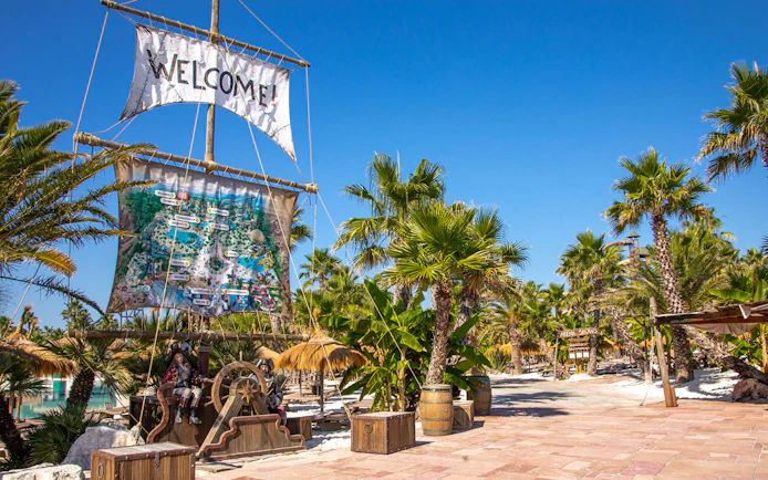 Caribe Bay entrance with pirate-themed decor and palm trees under a clear blue sky.