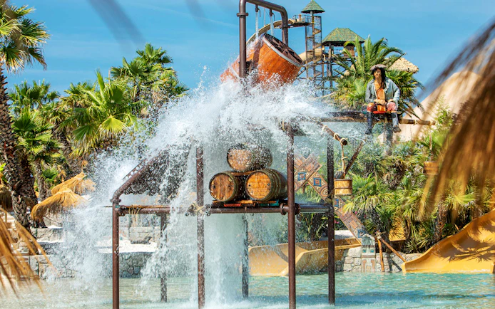 Water splash feature at Caribe Bay with palm trees and slides in the background.