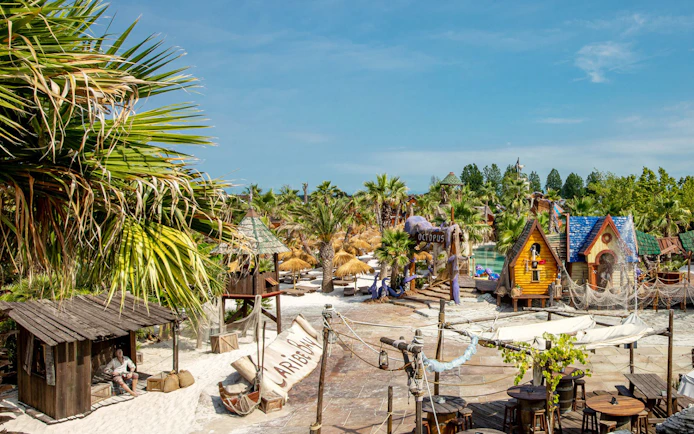 Caribe Bay entrance with tropical huts and palm trees in a water park setting.