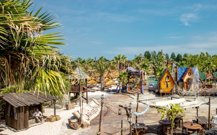 Caribe Bay entrance with tropical huts and palm trees in a water park setting.