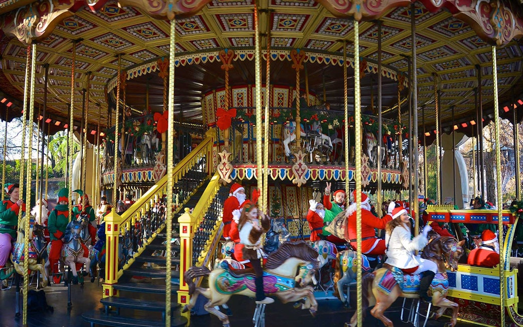 Carousel with festive decorations and people in holiday attire at Gardaland Park.