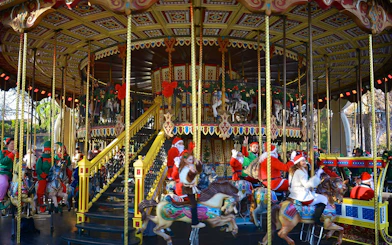 Carousel with festive decorations and people in holiday attire at Gardaland Park.