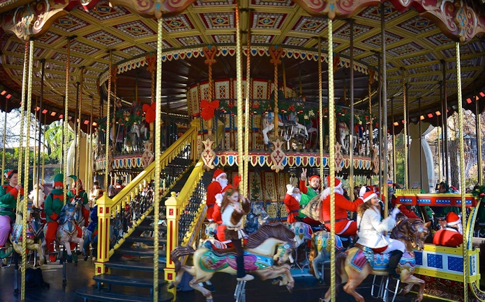 Carousel with festive decorations and people in holiday attire at Gardaland Park.