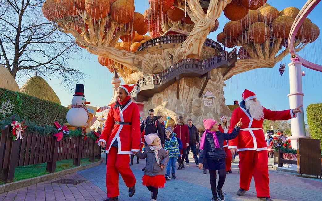 Visitors in festive attire at Gardaland Park with a large tree structure, Italy.
