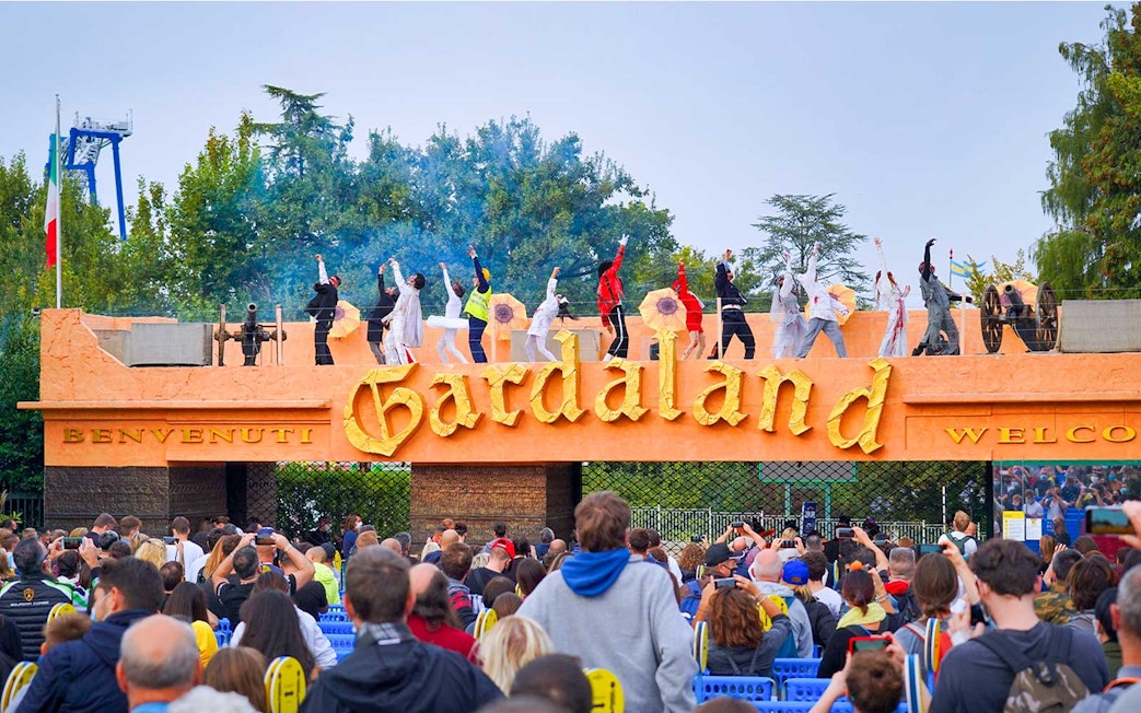 Performers on stage at Gardaland Park entrance, Verona, Italy, with a crowd watching.