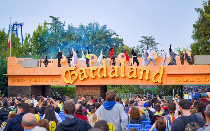Performers on stage at Gardaland Park entrance, Verona, Italy, with a crowd watching.