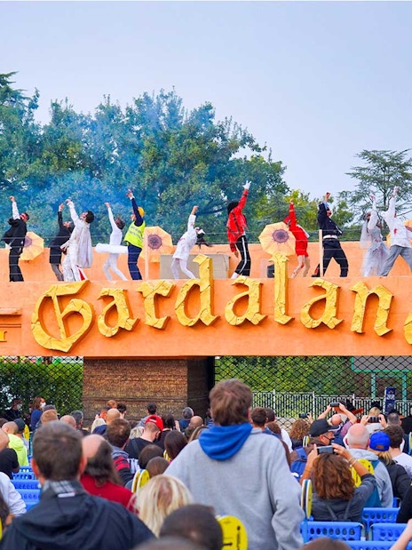 Performers on stage at Gardaland Park entrance, Verona, Italy, with a crowd watching.