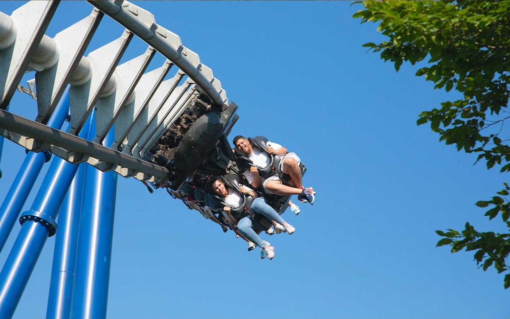 Roller coaster riders at Gardaland Park against blue sky.
