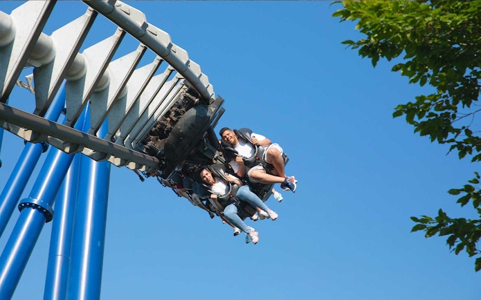 Roller coaster riders at Gardaland Park against blue sky.