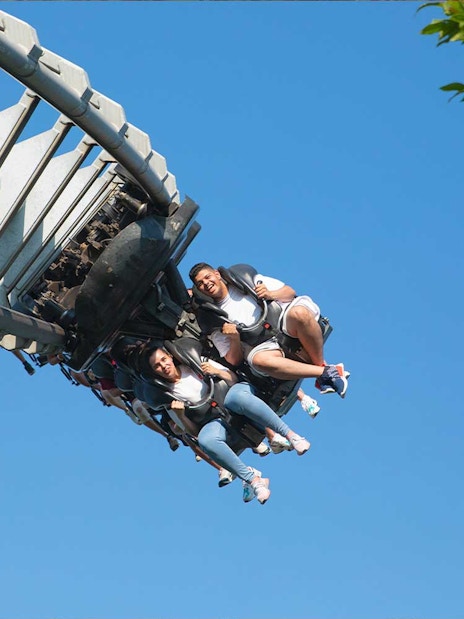 Roller coaster riders at Gardaland Park against blue sky.