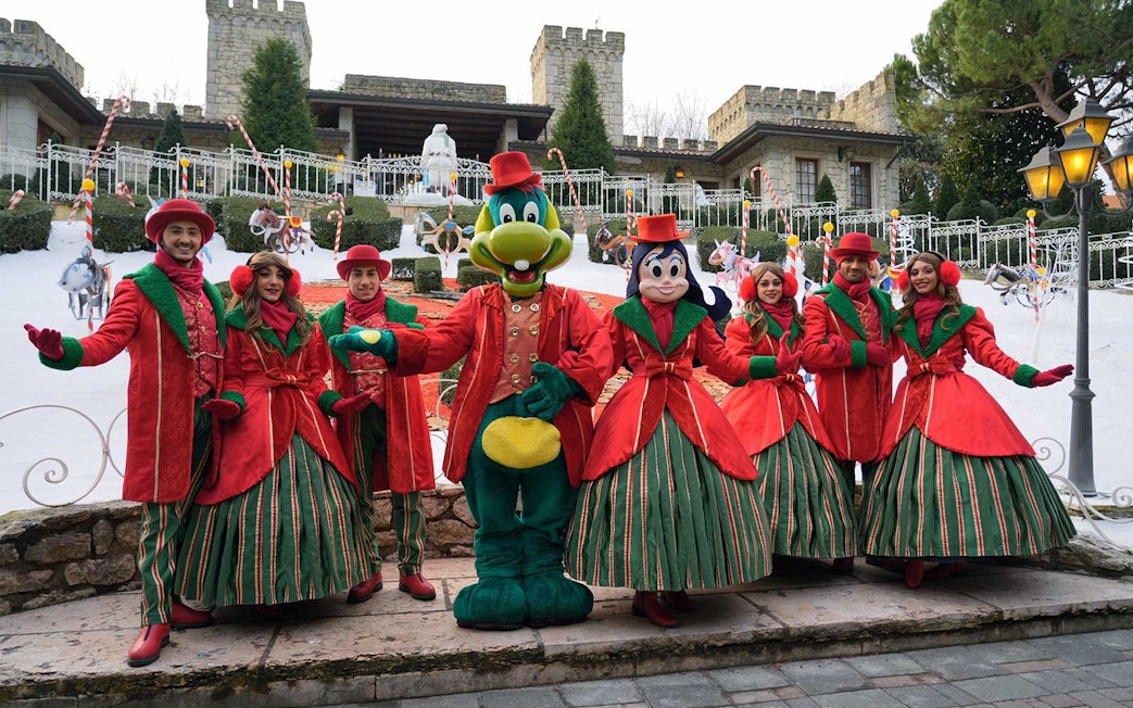 Characters in festive costumes at Gardaland Park, Italy, with a castle backdrop.