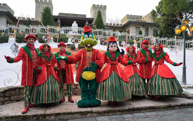 Characters in festive costumes at Gardaland Park, Italy, with a castle backdrop.