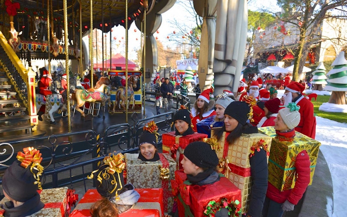 Visitors in festive costumes near a carousel at Gardaland Park during winter celebrations.