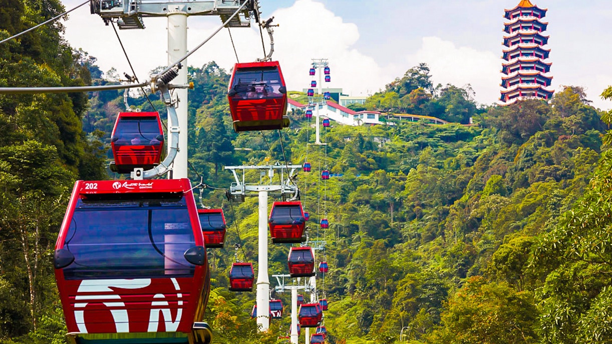 Genting Highlands cable cars ascending through lush green hills with a pagoda in the background.