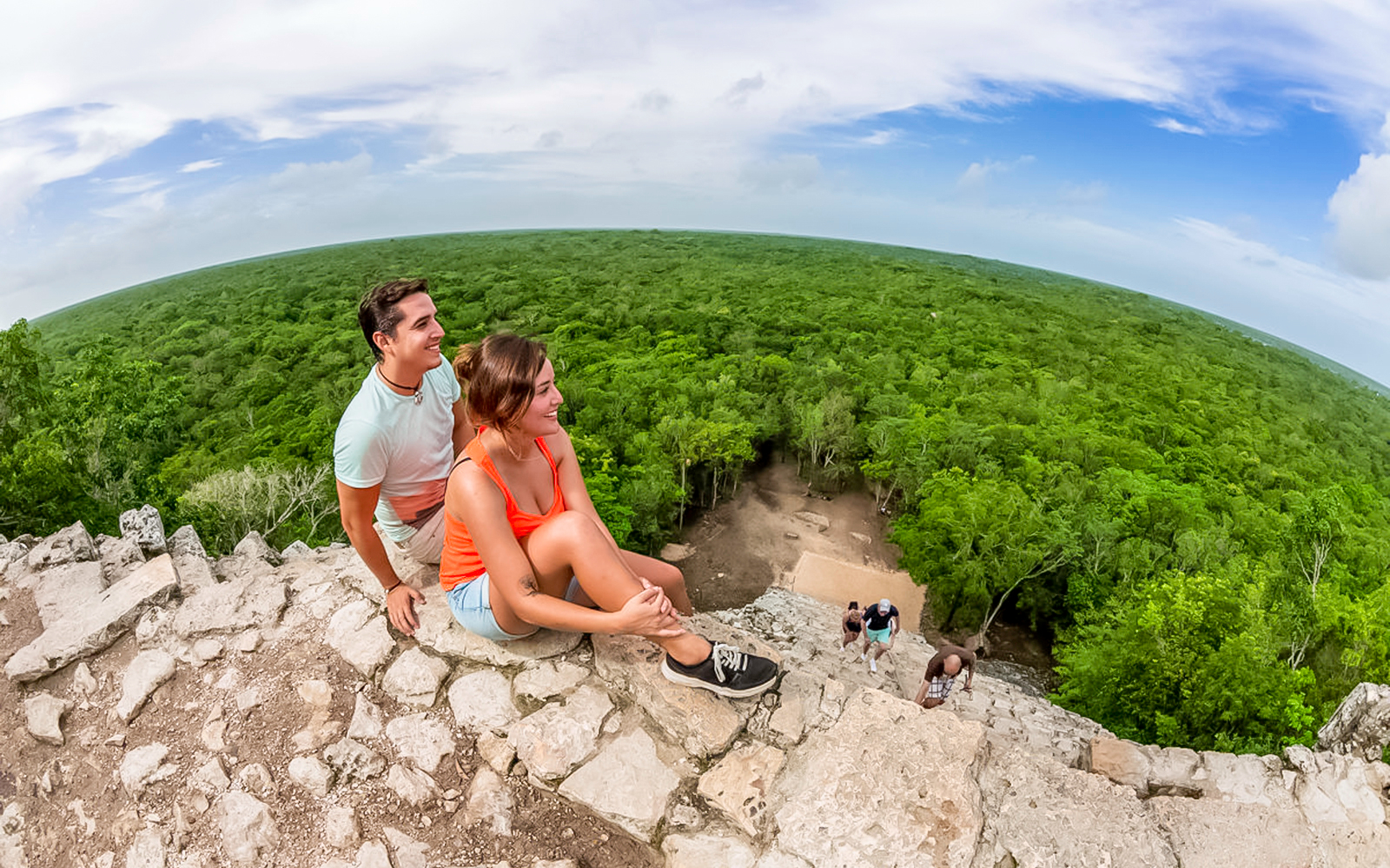 Visitors sitting atop the ancient Cobá pyramid overlooking lush jungle in Tulum, Mexico.