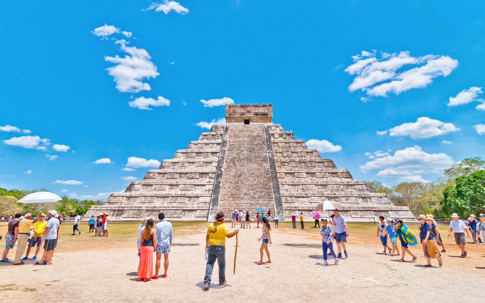 Tourists exploring the Pyramid of Kukulcán at Chichén Itzá under a clear blue sky.