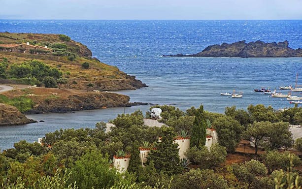 Cadaqués coastline with boats and Dalí's house surrounded by trees.