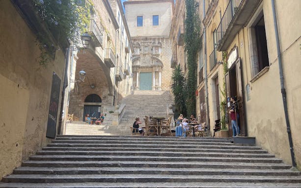Stone steps leading to historic buildings in Girona, with people dining outdoors.
