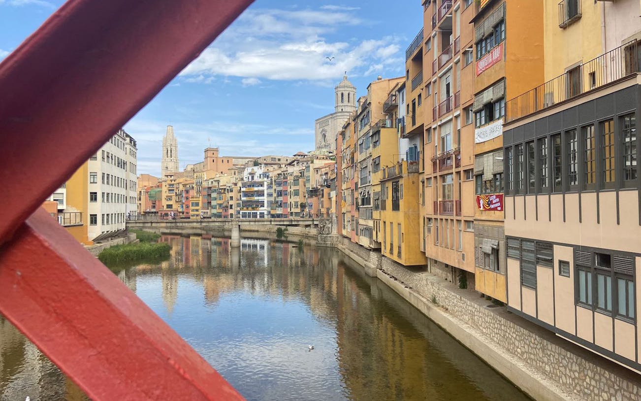 Colorful buildings along the Onyar River in Girona, viewed from a red bridge.
