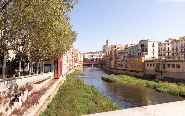 Colorful buildings along the Onyar River in Girona, with the Eiffel Bridge and cathedral in the background.