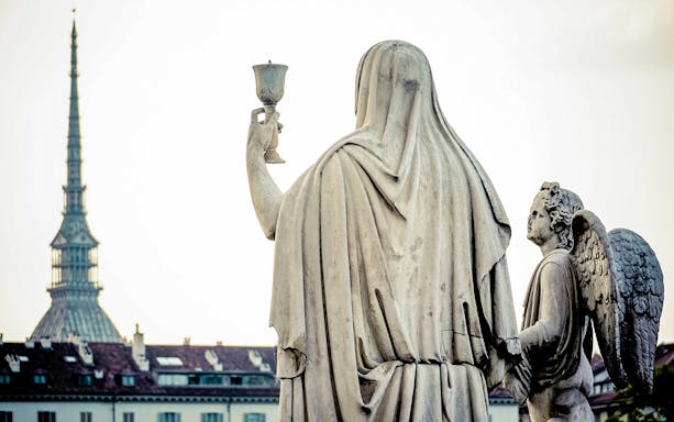 Statue holding chalice with angel in front of Mole Antonelliana, Torino Magica tour.