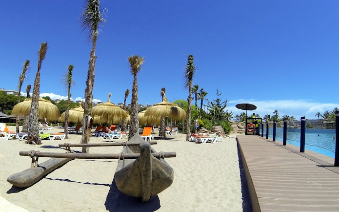 Aquopolis Costa Daurada beach area with straw umbrellas and sun loungers.