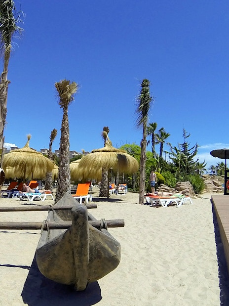 Aquopolis Costa Daurada beach area with straw umbrellas and sun loungers.