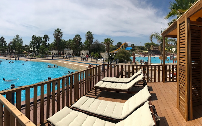 Sun loungers by the pool at Aquopolis Costa Daurada with water slides and palm trees in the background.