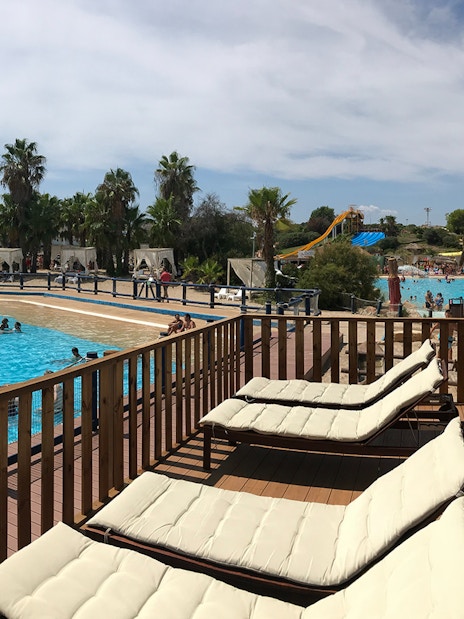 Sun loungers by the pool at Aquopolis Costa Daurada with water slides and palm trees in the background.
