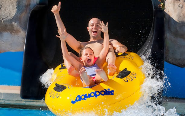 Father and child on a yellow raft sliding down a water slide at Aquopolis Cullera.