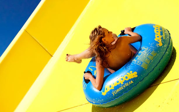 Person sliding on a yellow water slide at Aquopolis Torrevieja in a blue inflatable tube.
