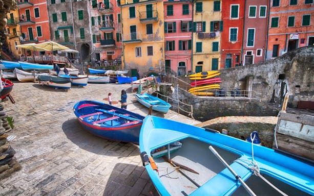 Colorful boats docked in Vernazza harbor, Cinque Terre, with vibrant buildings in the background.