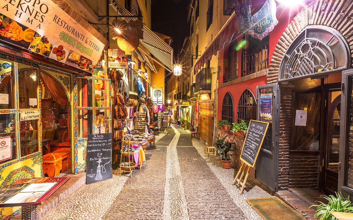 Narrow street in Granada with colorful shops and restaurants, part of the Alhambra and Cathedral tour.