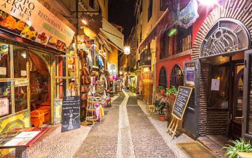 Narrow street in Granada with colorful shops and restaurants, part of the Alhambra and Cathedral tour.