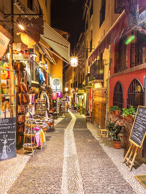 Narrow street in Granada with colorful shops and restaurants, part of the Alhambra and Cathedral tour.