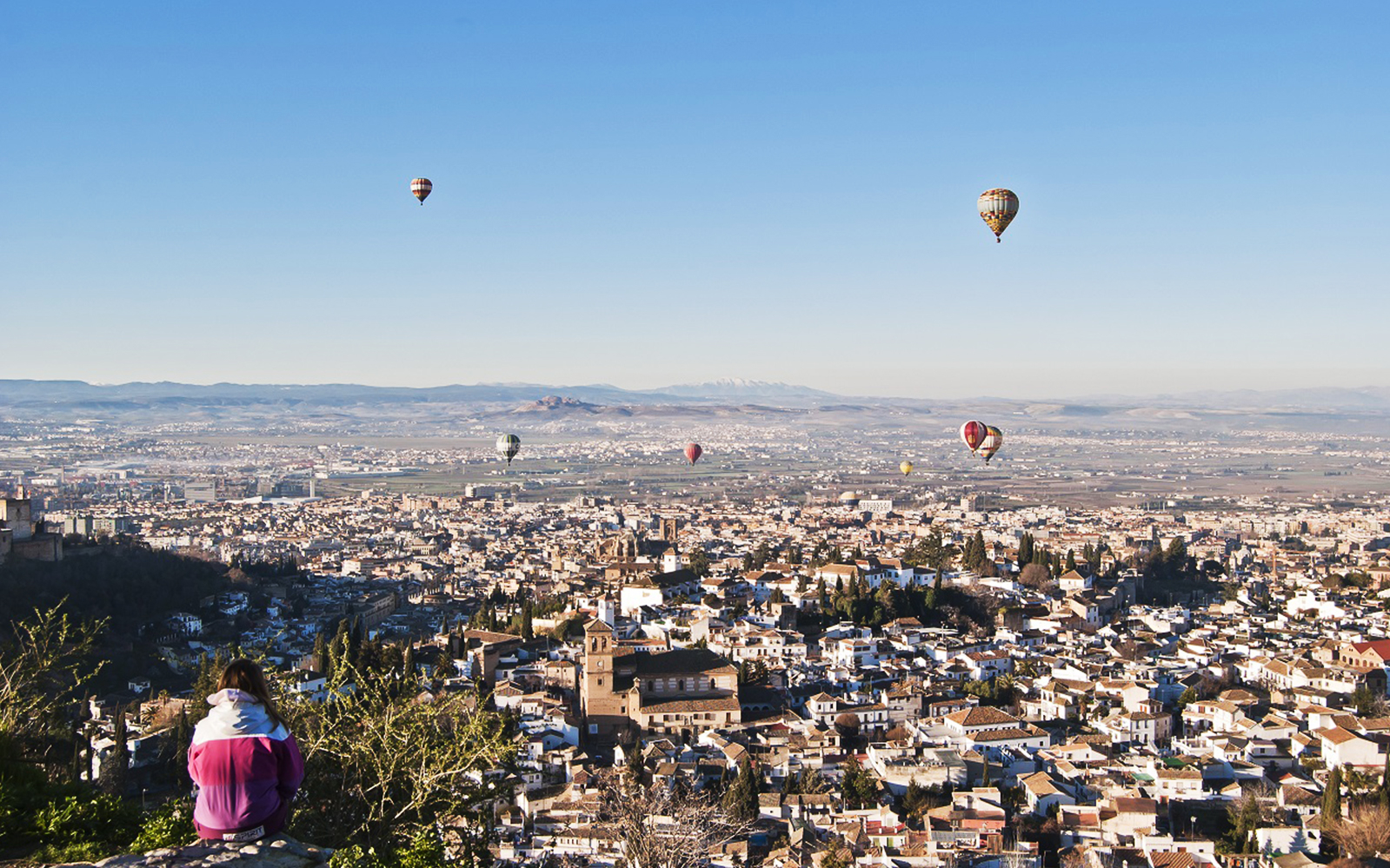 Hot air balloons over Granada with view of Alhambra and cityscape.