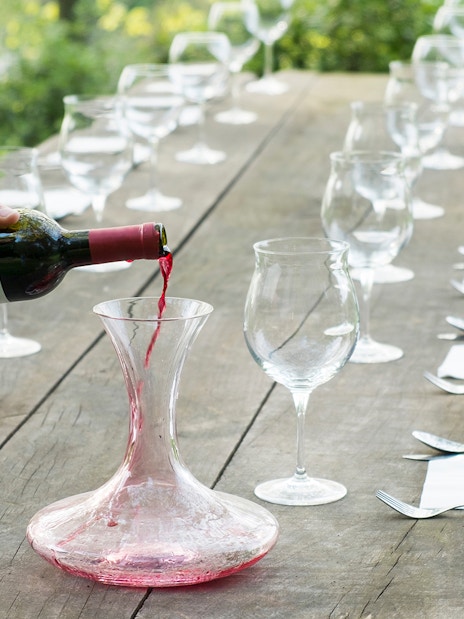 Pouring red wine into a decanter on a rustic table set for a Tuscany wine tour.