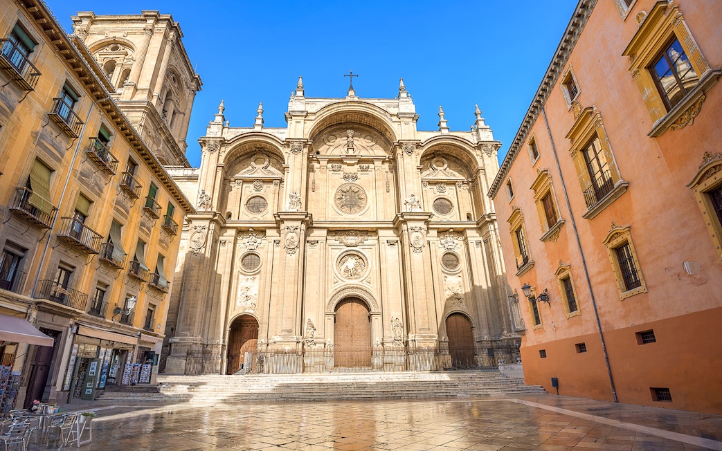 Cathedral and Royal Chapel of Granada facade with surrounding buildings in a sunny plaza.