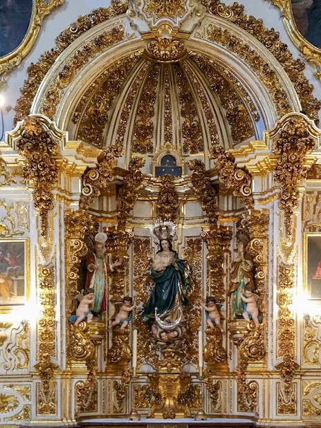 Ornate altar inside the Cathedral and Royal Chapel of Granada, featuring religious statues and gold detailing.