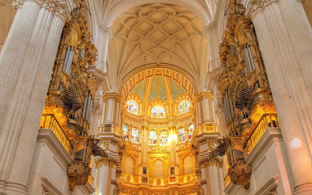 Interior view of Cathedral and Royal Chapel of Granada with ornate columns and stained glass windows.