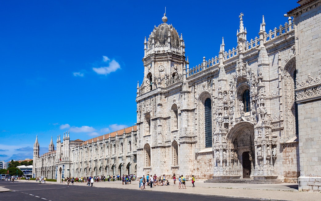 Jerónimos Monastery facade in Lisbon with tourists outside.