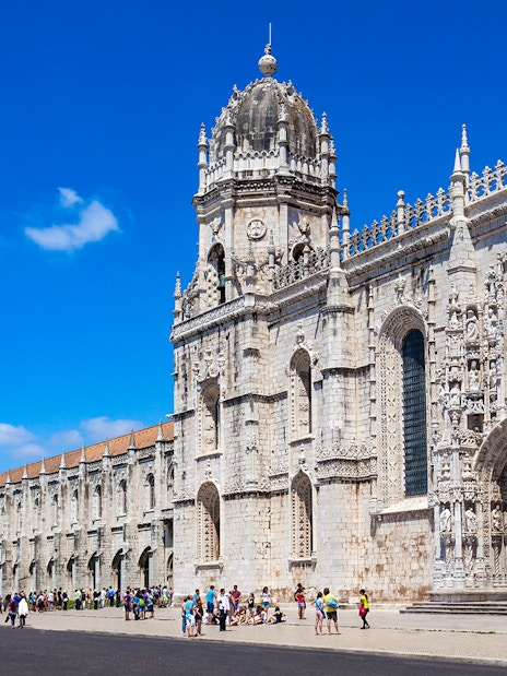 Jerónimos Monastery facade in Lisbon with tourists outside.