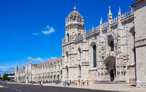 Jerónimos Monastery facade in Lisbon with tourists outside.