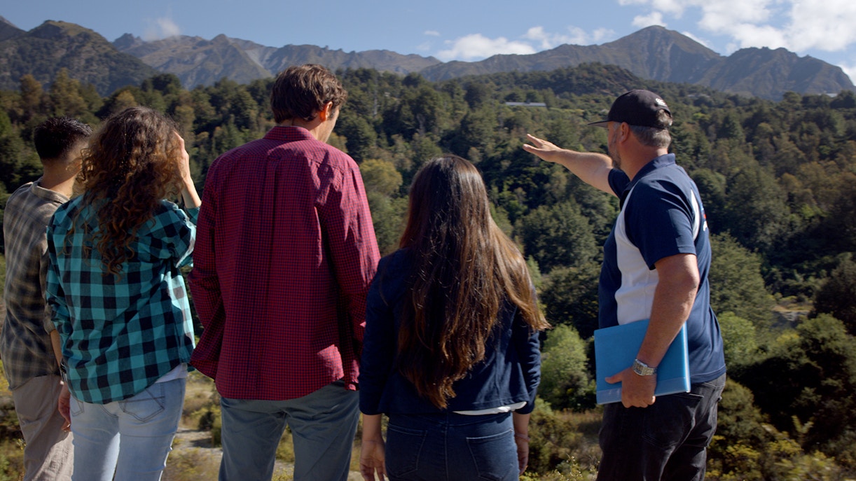 Tour guide pointing at scenic mountains during Lord of the Rings tour in Queenstown.