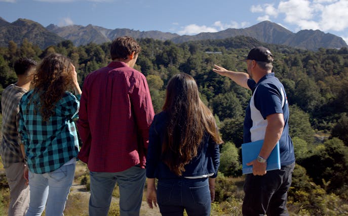 Tour guide pointing at scenic mountains during Lord of the Rings tour in Queenstown.