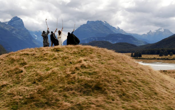 Group in costume on grassy hill with mountains, part of Lord of the Rings tour in Queenstown.