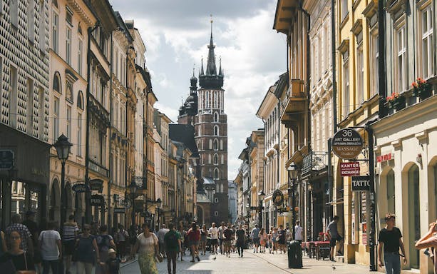 Krakow Old Town street with St. Mary's Basilica in the background, bustling with people.