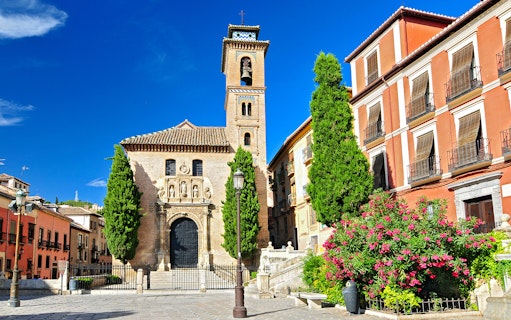 Cathedral facade with bell tower in Albaicin, Granada, surrounded by historic buildings.