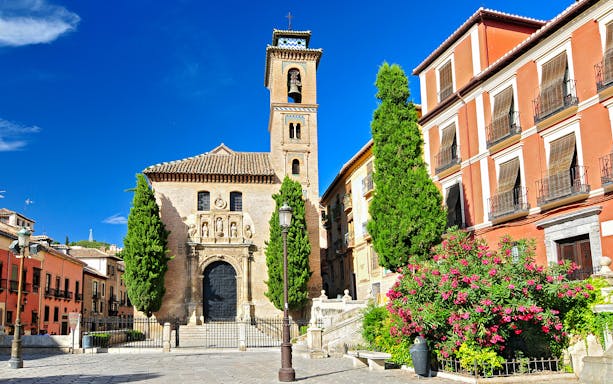 Cathedral facade with bell tower in Albaicin, Granada, surrounded by historic buildings.