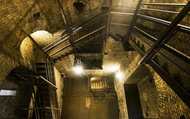 Underground passage with stone walls and metal stairs in Torino Noir tour, Italy.